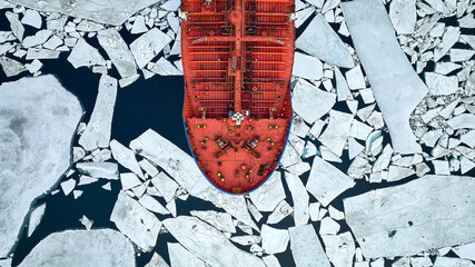 An orange-coloured tanker passes through thick ice in search of an icebreaker that will guide tankers through the arctic ice - obrazy, fototapety, plakaty