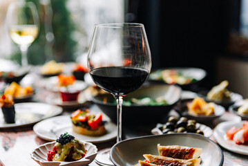glass with red wine and wine snack set, food from spain, cheese, meat, vegetables and other appetizers on table