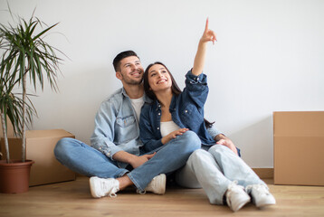 Happy Young Couple Sitting On Floor Among Cardboard Boxes After Moving