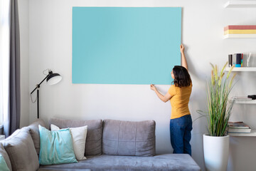 Young woman hanging large empty poster on the wall in living room