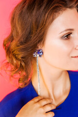 Beautiful long earrings on a young woman in a blue dress. Girl posing on a red fuchsia background