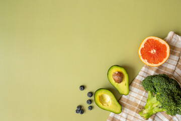 close-up, top view, healthy breakfast and nutrition: halves of avocado, broccoli, grapefruit and blueberries, beige napkin on a green background