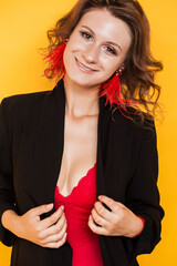Stylish brunette girl posing on an orange background in a sexy red top and black jacket with ostrich feather earrings
