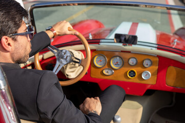 young man in convertible car looking at camera, smiling, man wears suit and tie drives red convertible car