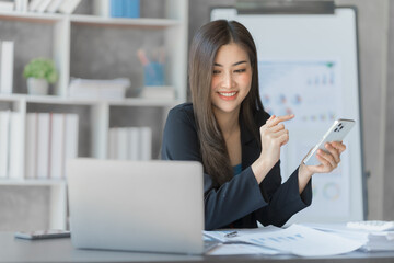 Beautiful Asian female bookkeeper doing online accounting with laptop in private accounting office, balance sheet and stock market statistics.