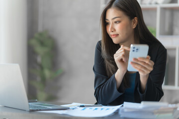 Beautiful Asian female bookkeeper doing online accounting with laptop in private accounting office, balance sheet and stock market statistics.