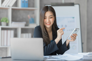 Beautiful Asian female bookkeeper doing online accounting with laptop in private accounting office, balance sheet and stock market statistics.