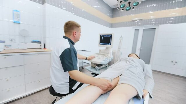 doctor does an ultrasound of the veins on the patient's legs. A phlebologist checks the veins on a woman's legs with an ultrasound machine in a modern clinic.