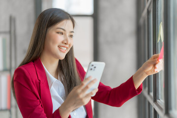 Pretty asia business woman bookkeeper brainstorming and working in modern office workplace with sticky notes or post it at windows.