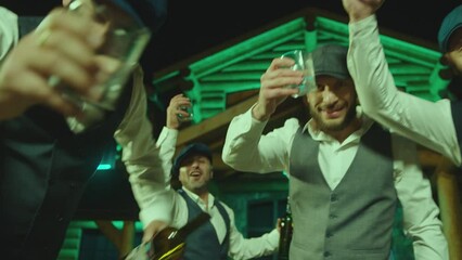 Group of young drunk men drinking alcohol , toasting , cheering , celebrating . Bachelor party with groom . Close up boys toasting on camera . Restaurant or house with led neon lights on background