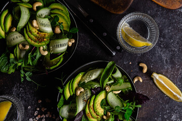 Salad of greens, cucumber and avocado on a dark table. Vegetarian dish