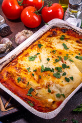 Homemade cannelloni pasta, big tray with haked cannelloni with minced meat with bechamel sauce,with herbs in ingrediant on dark background