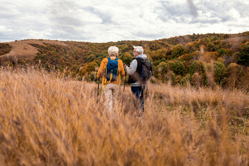 Active senior couple with backpacks hiking together in nature on autumn day.