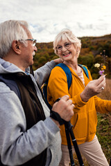 Active senior couple with backpacks hiking together in nature on autumn day.