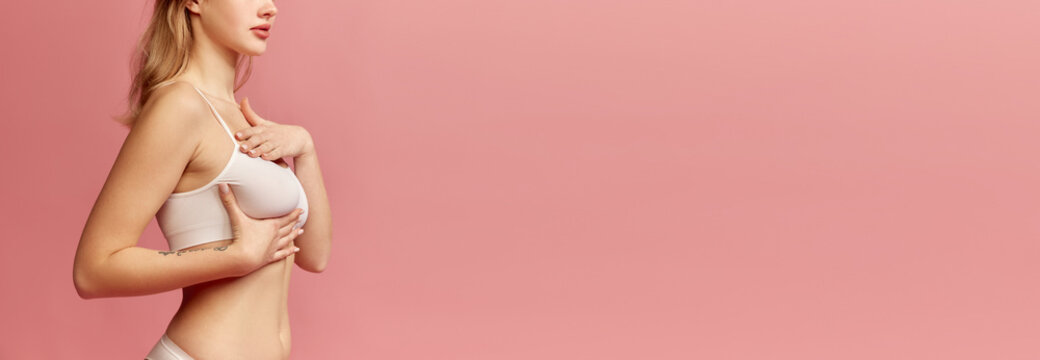 Cropped image of female body. Girl checking lumps on her breast for signs of breast cancer over pink background. Women healthcare, mammography concept.
