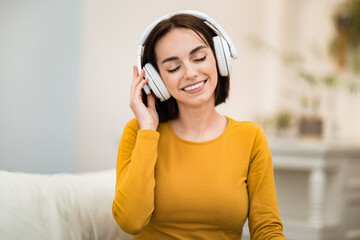 Joyful young woman listening to music, using wireless headphones