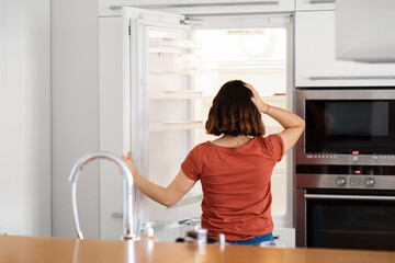 Young Woman Looking Inside Of Empty Fridge With No Food, Rear View