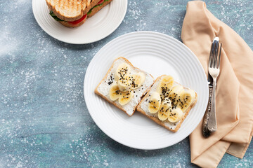 Sandwich breakfast has banana cream cheese sesame on blue wood table.