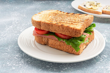 Sandwich breakfast has ham cheese and tomato vegetable on blue wood table.