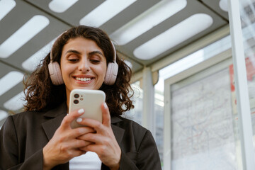 Young woman in headphones smiling and using mobile phone