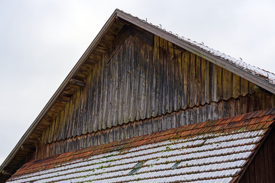 Close-up of snow covered roof with tiles and wooden wall at City of Zürich district Schwamendingen on a gray and cloudy winter day. Photo taken January 29th, 2023, Zurich, Switzerland.