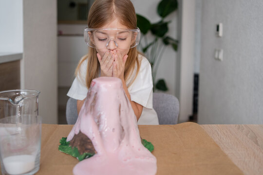Homeschooling concept. Kid in protective glasses having fun making DIY volcano model eruption for school science project homework.