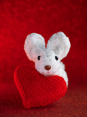 a white knitted bunny and a red heart on a red background. valentine's day greeting card