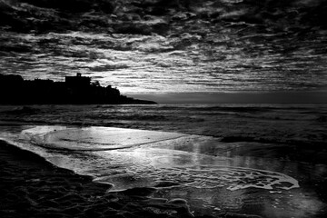 Dramatic black and white sea landscape image with dark sky and white waves. City in background....