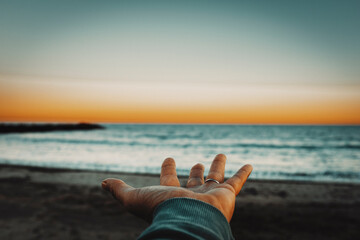 Fototapeta na wymiar Pov of man hand opened and beautiful sunset lights with ocean and sky in background. Focus in foreground. Concept of mankind and nature. People and travel adventure lifestyle. Feeling. Love. Sea.