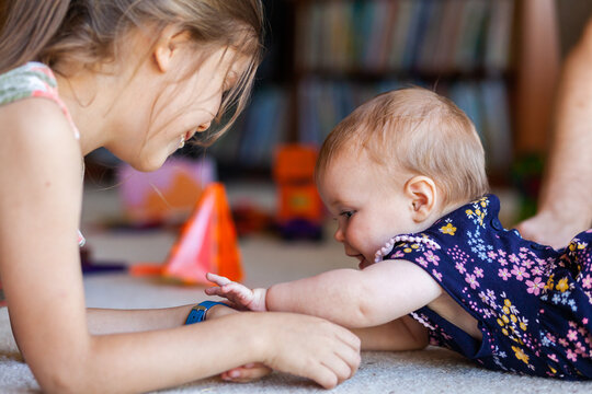baby playing with older girl on the floor reaching for watch