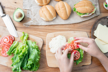 A young woman is putting some tomatoes on a healthy sandwich with lettuce and avocado