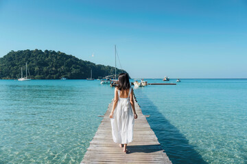Young asian woman in white dress walking on wooden pier in tropical sea on sunny day