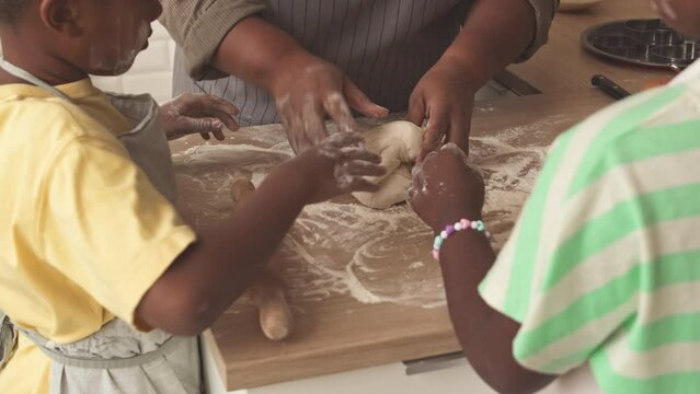 Grandmother and her two helpful grandchildren kneading handmade dough on kitchen table together