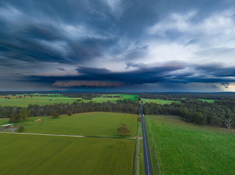 Aerial view of a narrow country road running between green farmland and under a dark stormfront
