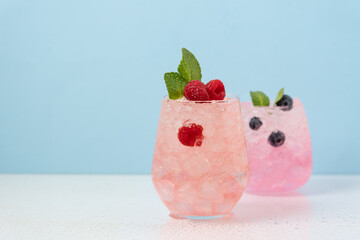 Berry drinks with ice in glasses on blue background. Refreshing tropical summer berry lemonade or...
