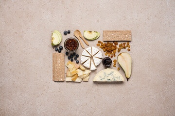 Creative cheese platter. Variety soft and hard cheeses, fruit, jam on beige concrete background....