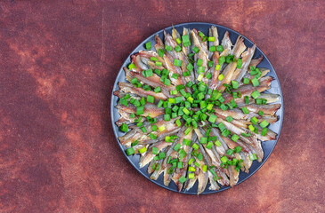 european anchovy fish fillet  with green onion in a black plate on a red brown leather background...
