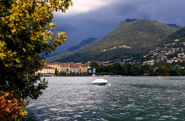 Landscape view of Lake Lugano, embankment with buildings and mountains in the background against a stormy sky in the city of Lugano in southern Switzerland