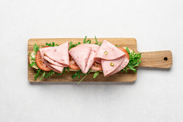 Italian style sandwich with arugula, mortadella ham and tomatoes. Baguette toast on wooden board on...