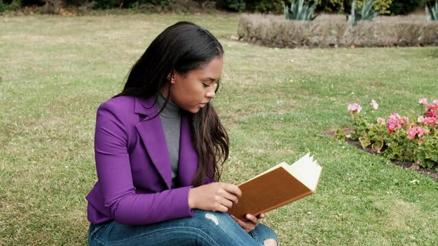Young woman is reading a book sitting on the grass.