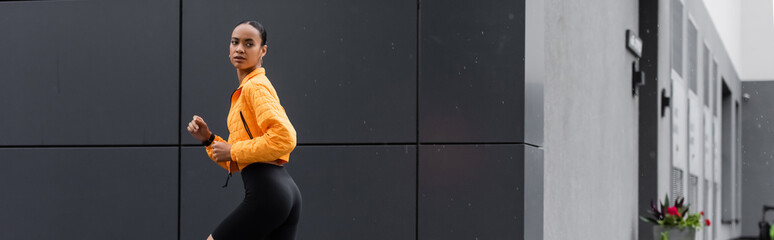 brunette african american sportswoman in bike shorts and yellow puffer jacket running outside, banner. © LIGHTFIELD STUDIOS