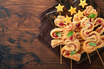 Christmas or New Year appetizer. Christmas tree shape puff pastry buns with cheese and ham. Group of Christmas tree shapes on wooden board. Festive idea for Christmas or New Year dinner. Top view.
