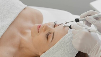 A beautiful woman receives a microcurrent facial skin treatment from cosmetologist in a spa salon. Doctor uses electrical pulses for cosmetic procedures to smooth out wrinkles, restore and rejuvenate
