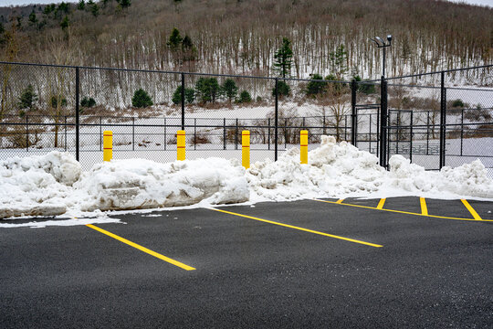 4 Large Yellow Concrete Pillars are placed on the edge of the parking lot to protect the Tennis Court fences from being damaged during snow plowing in the winter in Upstate NY.