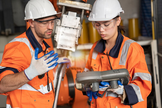 Asian Male Engineer And Female Programmer Examining The Operation Of A Smart Industrial Robotic Arm For Digital Factory Manufacturing Technology.