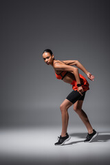 full length of young african american woman in sneakers posing while training on grey.