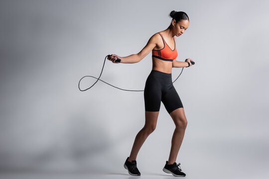 full length of sportive african american woman exercising with skipping rope on grey.