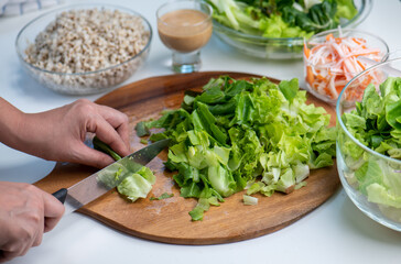 Hand cut and slice fresh baby cos salad on wood board table .Organic Vegetables mix lunch with green vegetables at kitchen table on wood cutting board.
