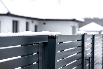 Modern anthracite panel fence with falling snow, visible sliding gate.