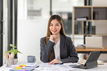 Young business Asian woman is sitting at table, working on laptop with graphs, charts, money and report financial concepts. Online marketing, education, analytics, e-commerce, business planning